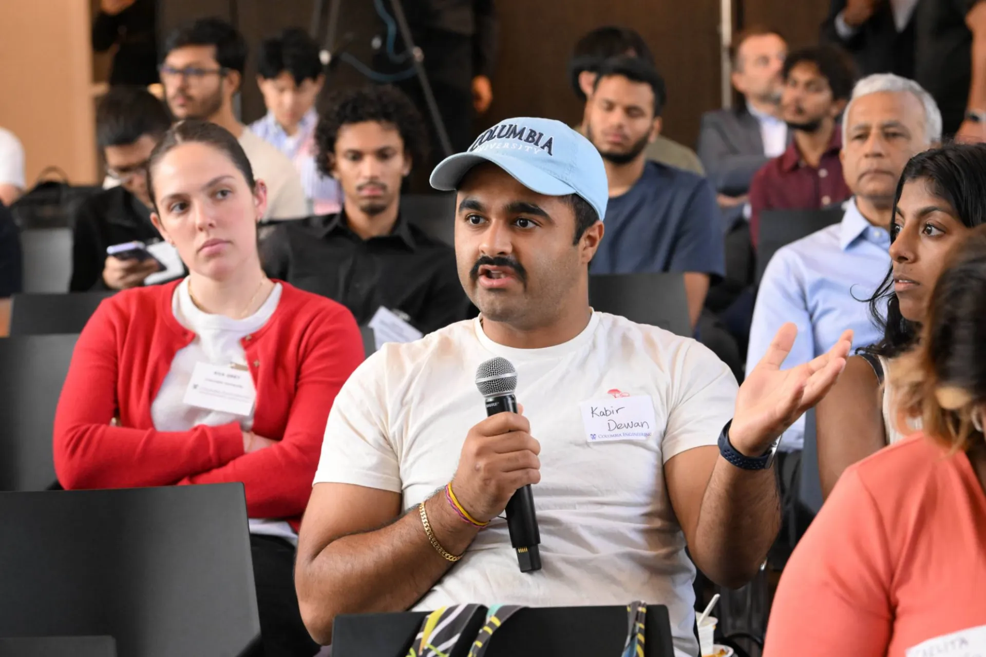 image of an audience member in a light blue columbia hat, speaking into a handheld microphone