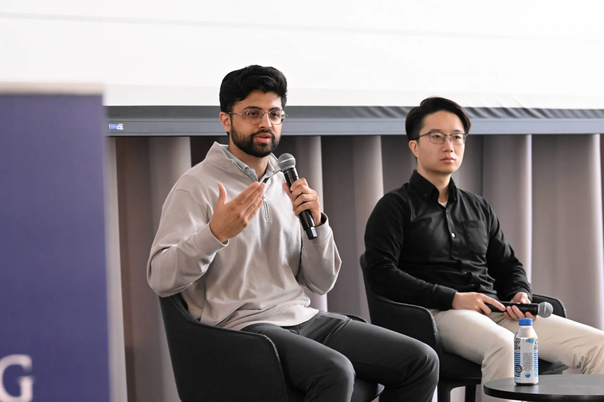 image of 2 panelists, the one on the left speaking into a handheld microphone gesturing to an audience