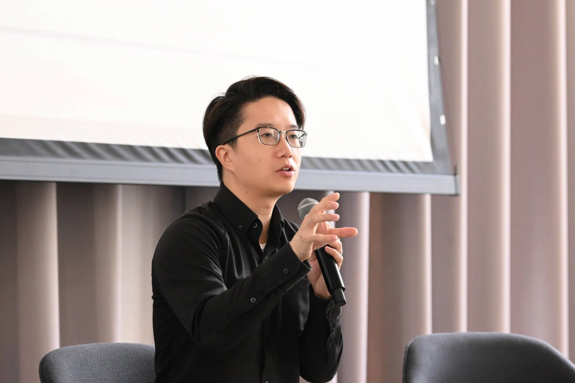 panelist in all black outfit speaking into a handheld microphone gesturing to an audience