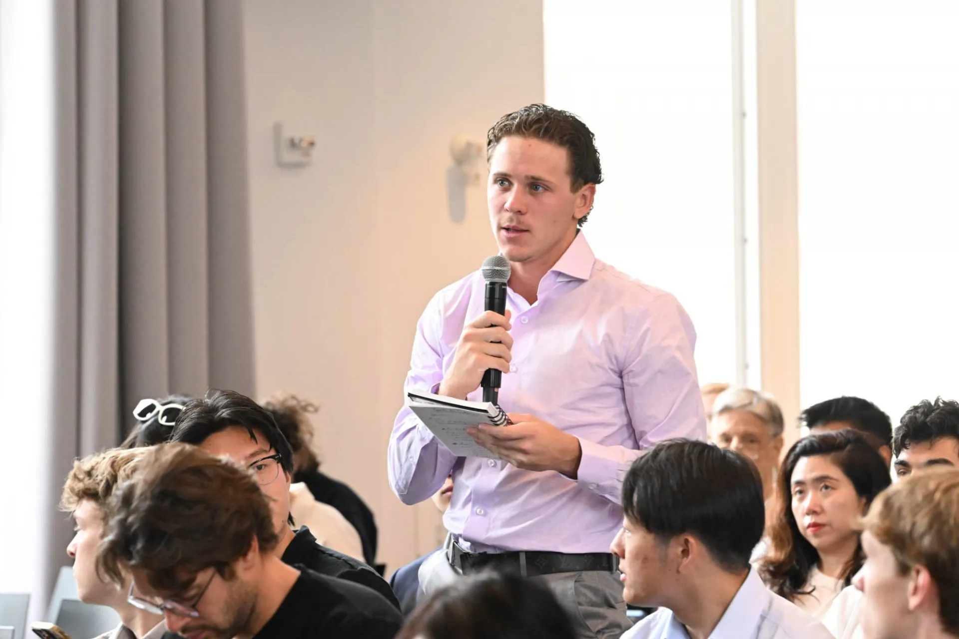 image of audience member wearing a light colored button down standing up from the crowd, speaking into a microphone in hand